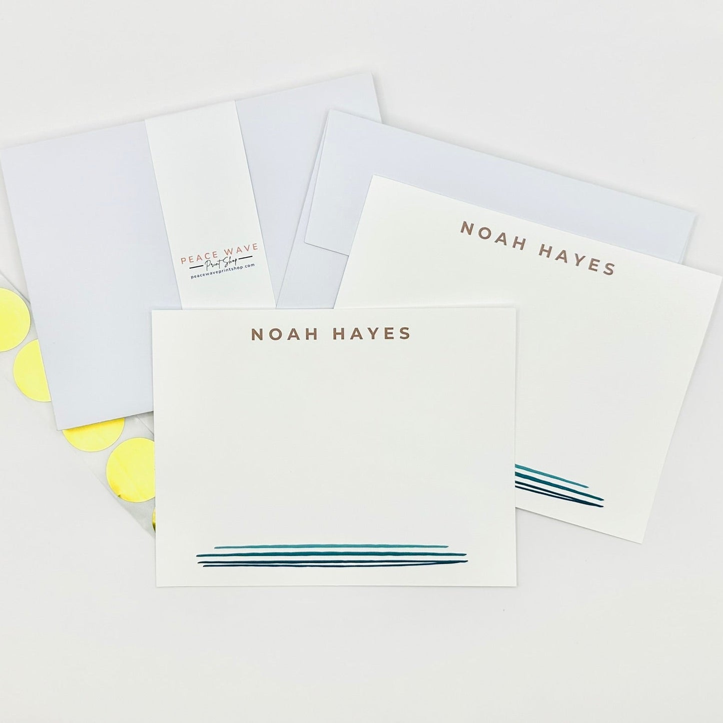 Set of stationery items with personalized name 'NOAH HAYES' and blue watercolor line design and gold envelope sticker seals on a light background