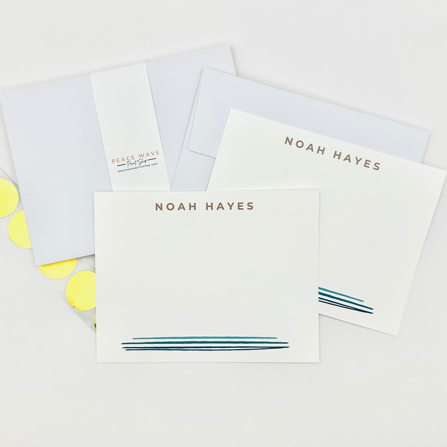 Set of stationery items with personalized name 'NOAH HAYES' and blue watercolor line design and gold envelope sticker seals on a light background