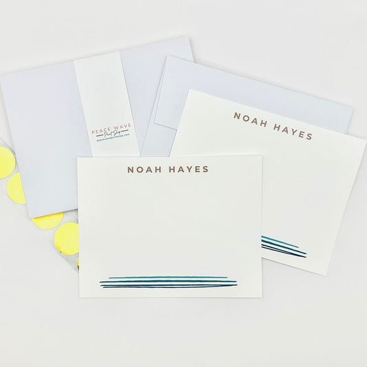 Set of stationery items with personalized name 'NOAH HAYES' and blue watercolor line design and gold envelope sticker seals on a light background