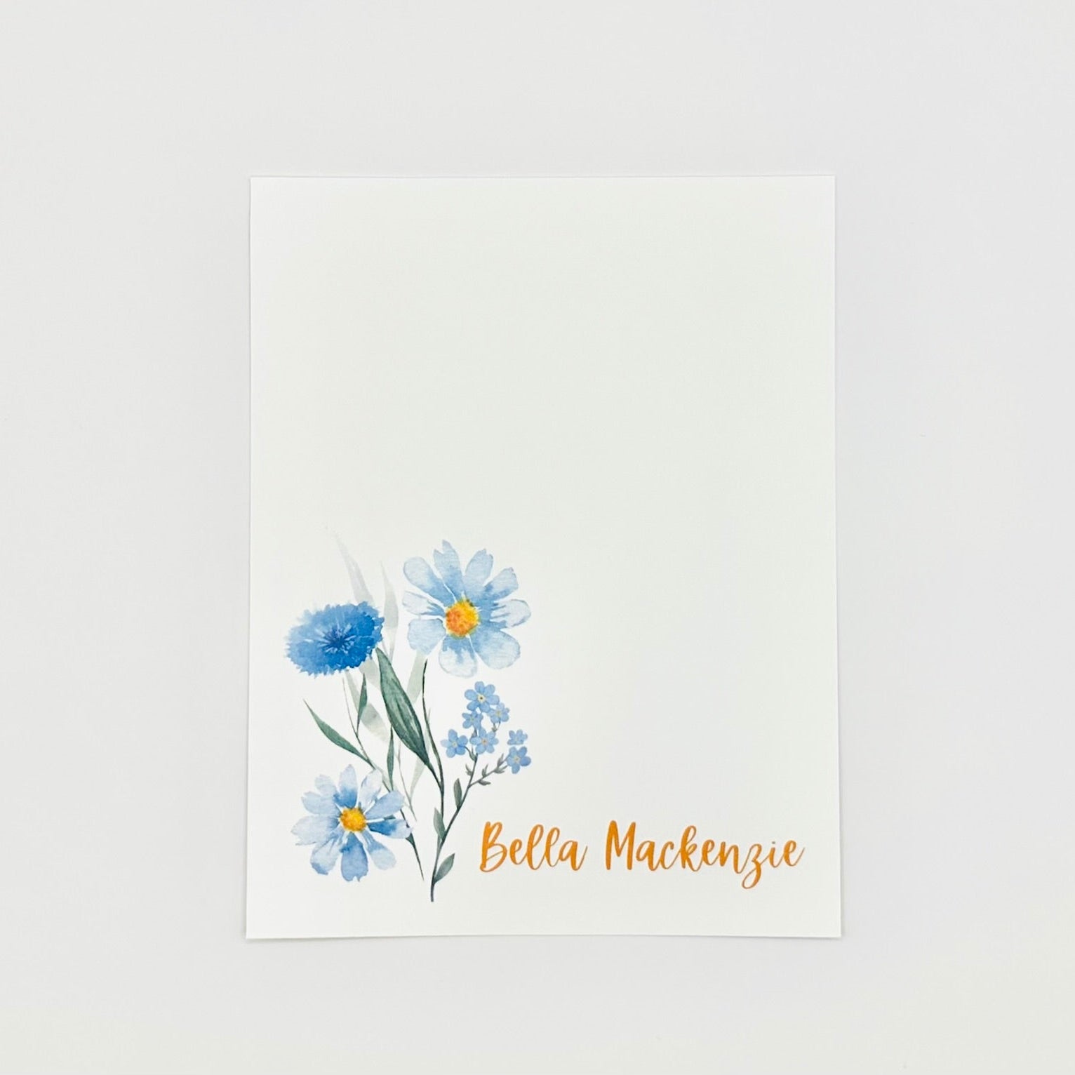 Stationery flat card with blue floral design personalized with name 'Bella Mackenzie' on a white background