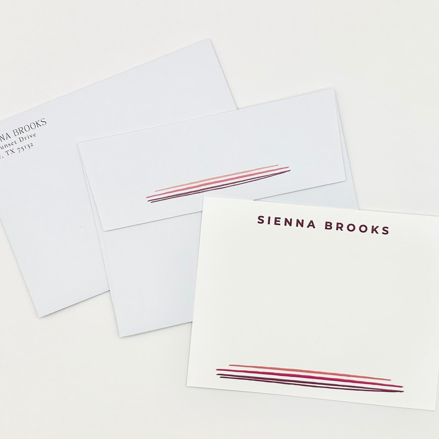 Set of stationery flat cards and coordinating envelopes with personalized name 'Sienna Brooks' and pink watercolor lines on a white background with return address printed on envelope