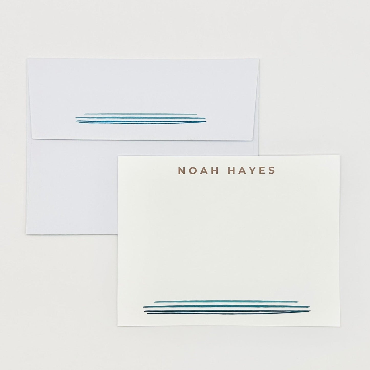 White stationery set personalized with 'NOAH HAYES' and watercolor blue line design printed on a card with coordinating envelopes against a white background